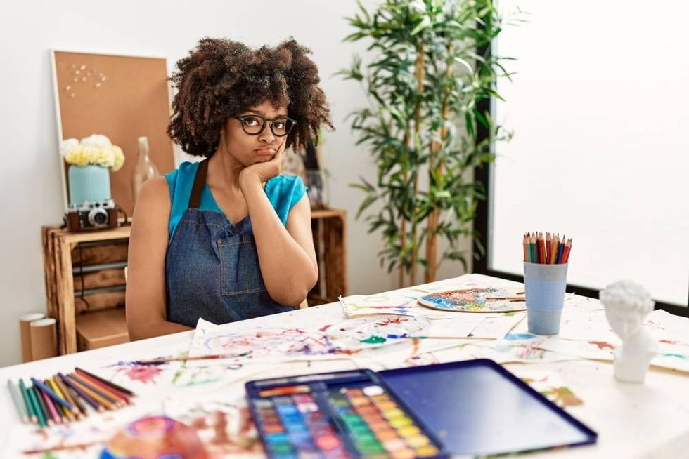 Frustrated Artist sitting at her desk in a studio setting with art supplies in front of her.
